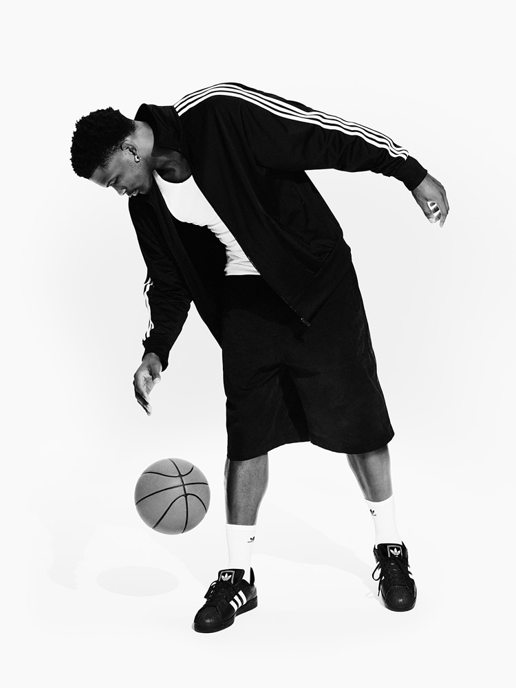 Anthony Edwards wears a black adidas Firebird jacket and matching shorts. He dribbles a basketball while wearing white socks with the Trefoil logo and black adidas Superstar sneakers.