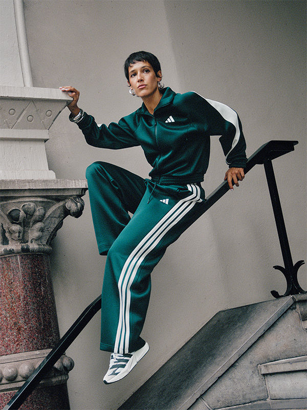 A person wearing a green and white tracksuit is standing on a set of stairs, with a stone structure in the background.