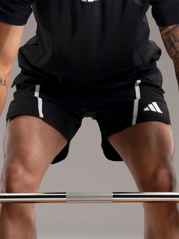 The image shows the lower body of a person wearing black athletic shorts with white stripes, standing on a gray surface.