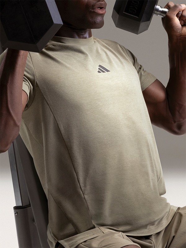 The image shows a person wearing a beige t-shirt, standing in front of a dark background.