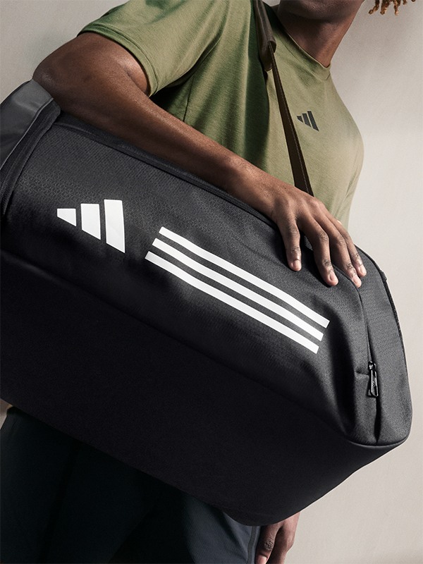 A person in a green shirt is holding a black and white sports bag with stripes on it.