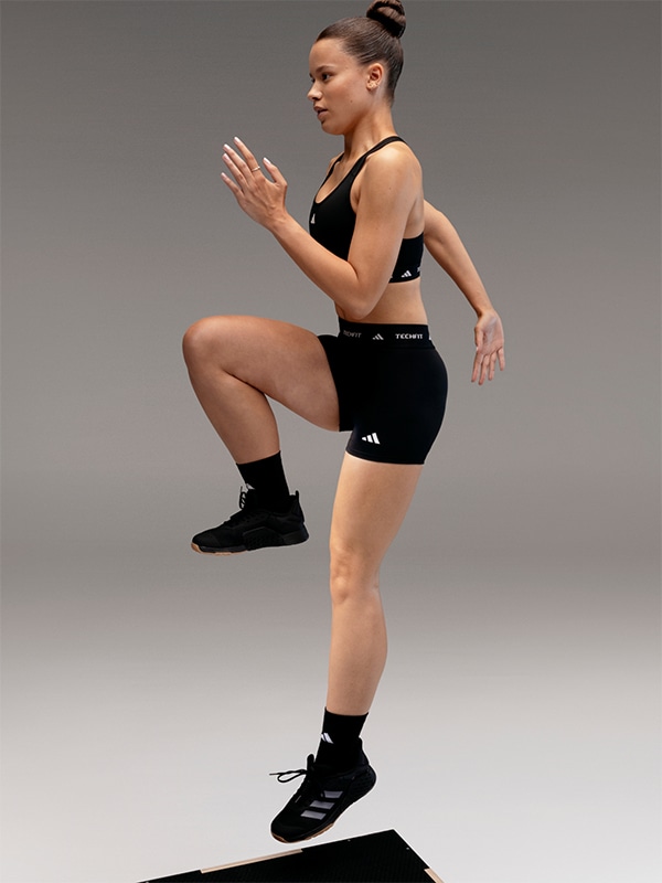 A person in athletic attire is performing a squat exercise on a plain gray background.