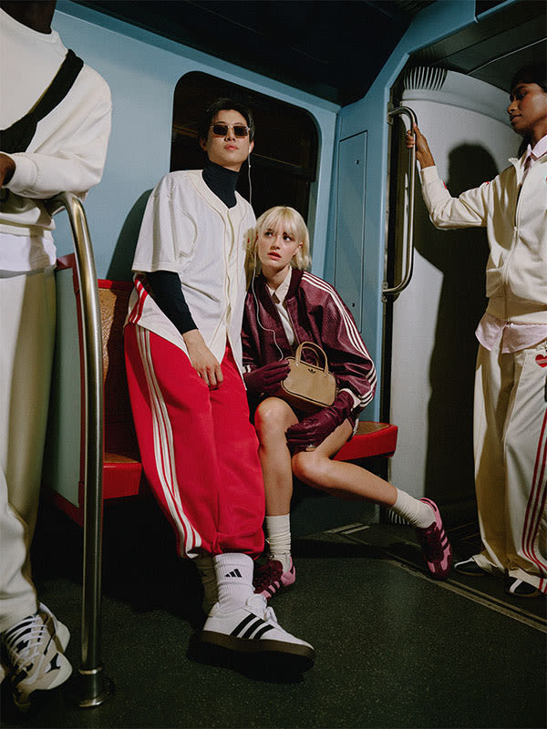 The image depicts two individuals, a person wearing a white jacket and a person wearing a red jacket, sitting in what appears to be the interior of a vehicle or transportation mode.