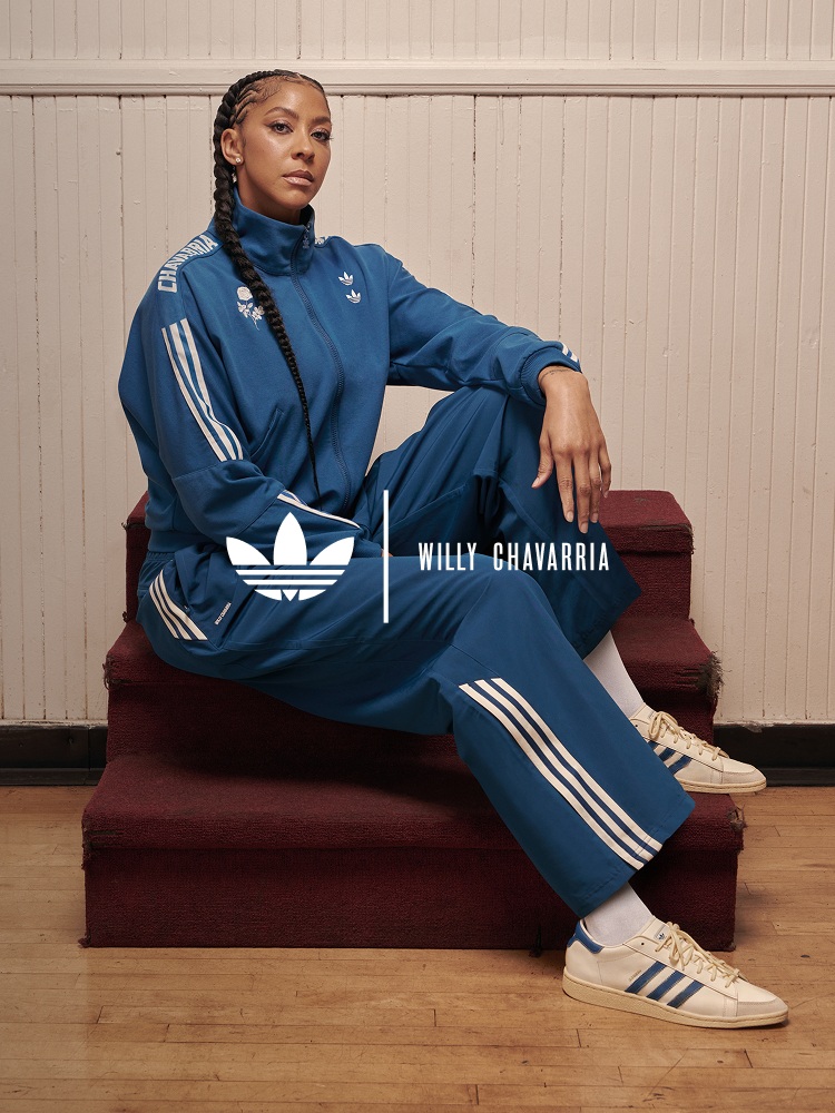 A person wearing a blue Adidas tracksuit is sitting on a red couch against a wooden paneled wall.