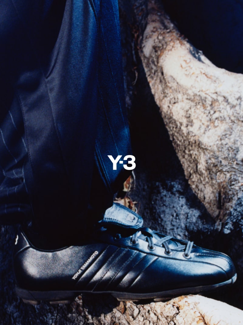 The image shows a close-up view of a black and blue athletic shoe with the "Y-3" logo prominently displayed, set against a dark, rocky background.