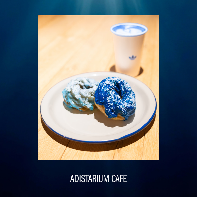 The image shows two pastries on a plate, one with a blue glaze and the other with a lighter color, accompanied by a cup of what appears to be coffee or tea on a wooden table.
