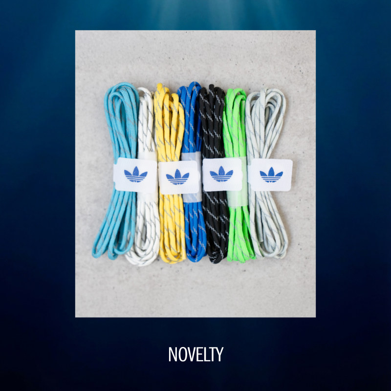 The image shows a collection of colorful shoelaces or laces in various shades of blue, yellow, black, and green, neatly arranged and packaged in Adidas-branded containers against a plain, light-colored background.