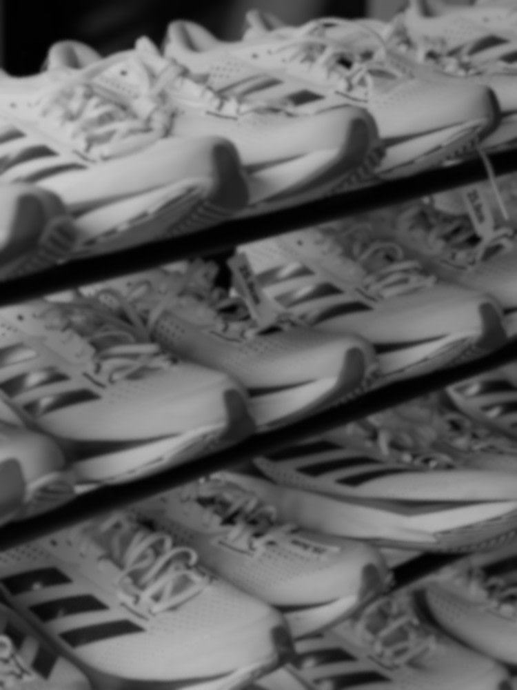 A black and white image depicting a collection of various sneakers or athletic shoes arranged in a disorganized manner, with the shoes overlapping and scattered across the frame.