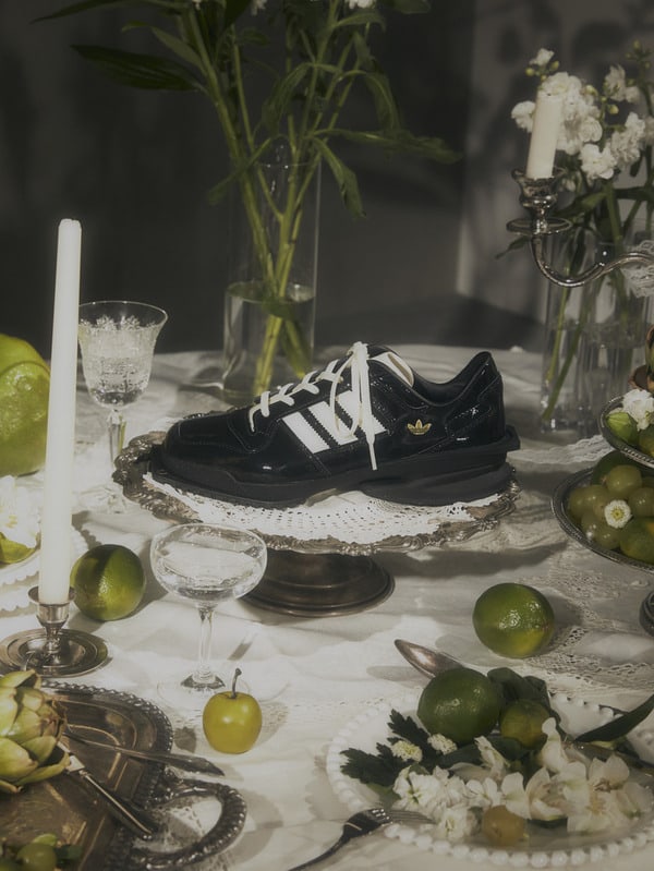 A pair of black and white sneakers sits on a wooden pedestal surrounded by various fruits, flowers, and glassware on a table.