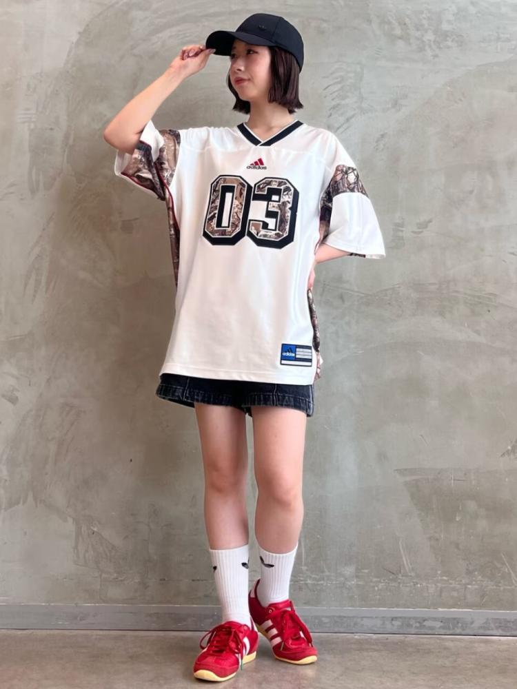 A young person wearing a white jersey with the number "03" printed on it, standing in front of a gray concrete wall and wearing red sneakers.