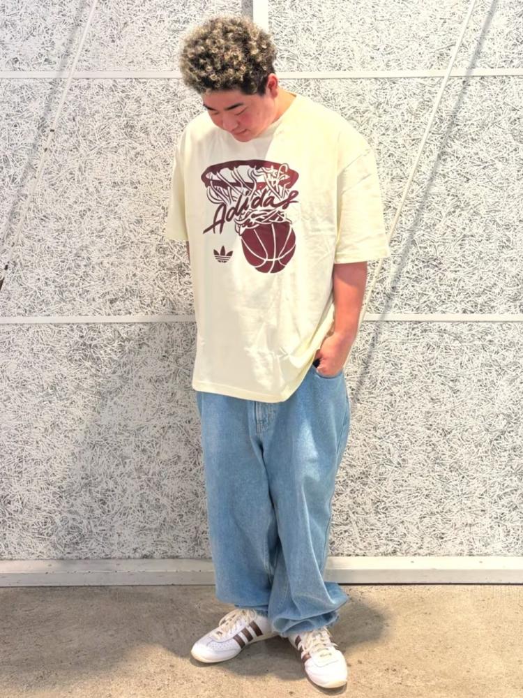 A young person wearing a white t-shirt with a graphic design and standing in front of a tiled wall.