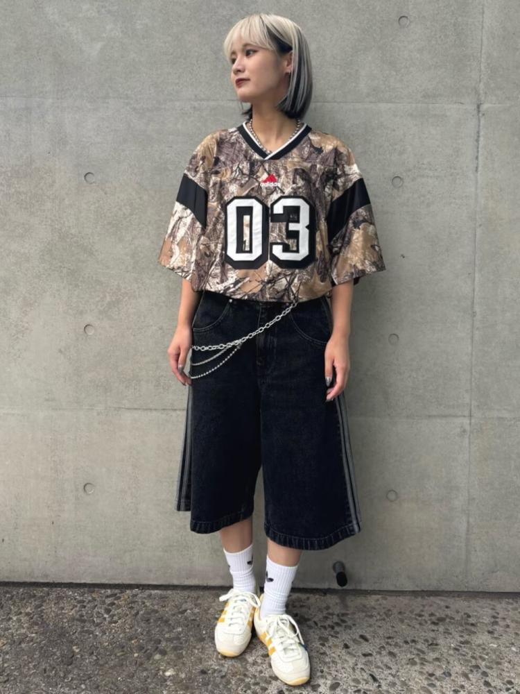 A young person wearing a camouflage-patterned jersey with the number "03" on it, standing in front of a concrete wall.