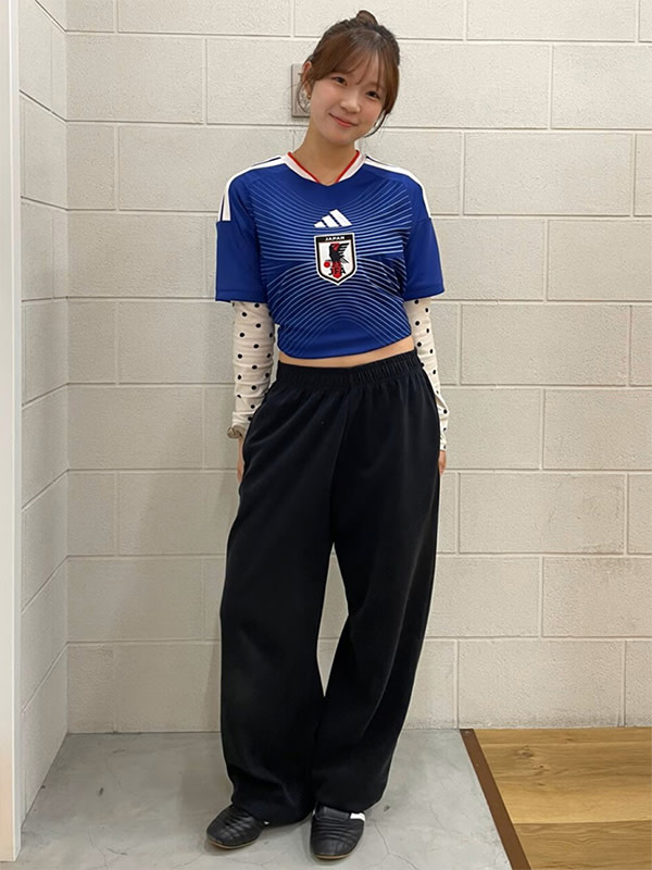 A young woman wearing a blue and white striped jersey and black pants stands in a room with white tiled walls.