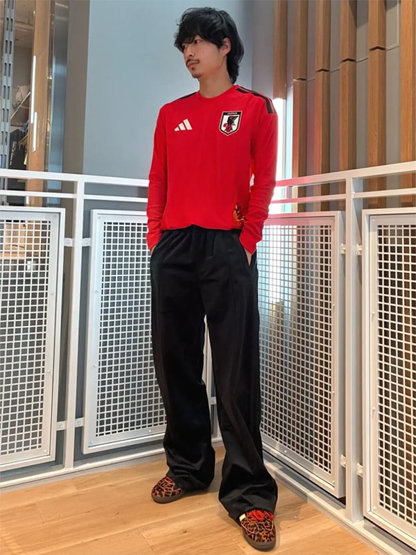 A person wearing a red jersey and black pants stands in a hallway with a metal grate in the background.