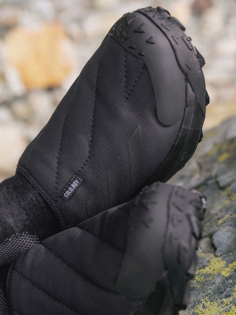 A close-up view of a pair of black, insulated gloves resting on a mossy, rocky surface.