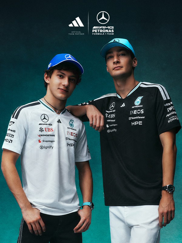 Two young men wearing Mercedes-AMG Petronas Formula One team uniforms and caps, standing together in front of a green background with the team's logos.