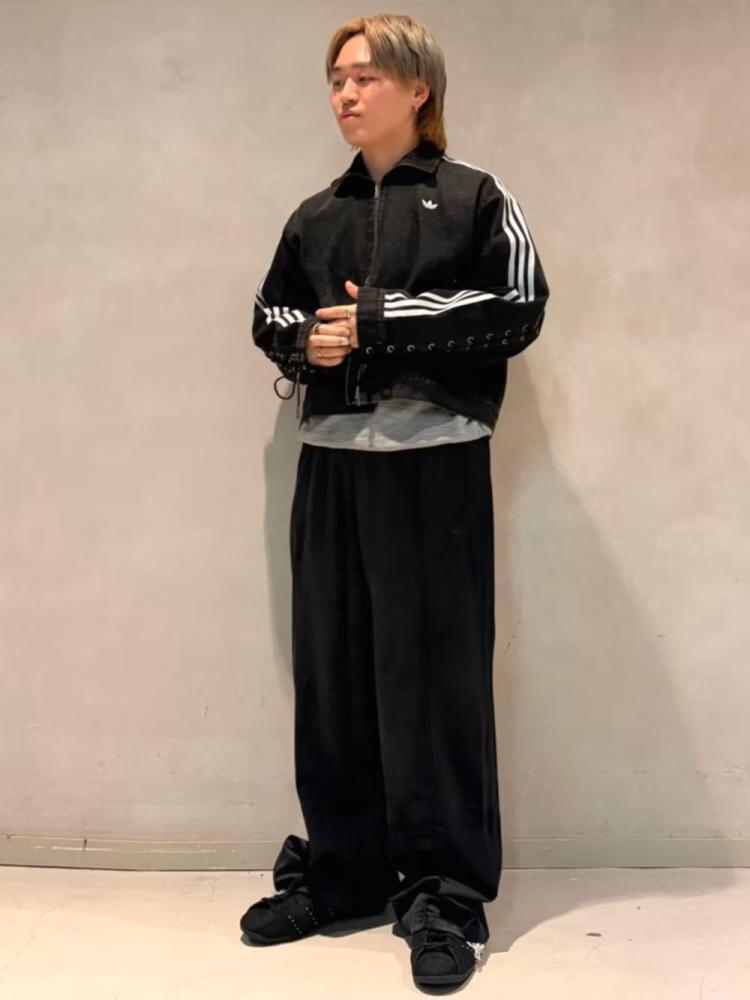The image shows a person wearing a black and white athletic jacket and pants, standing in front of a plain white wall.