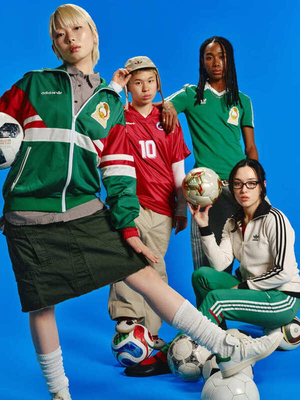 A group of diverse individuals, including a young boy wearing a red jersey, a woman in a green tracksuit, and a man with dreadlocks, are posing together with soccer balls and equipment against a vibrant blue background.