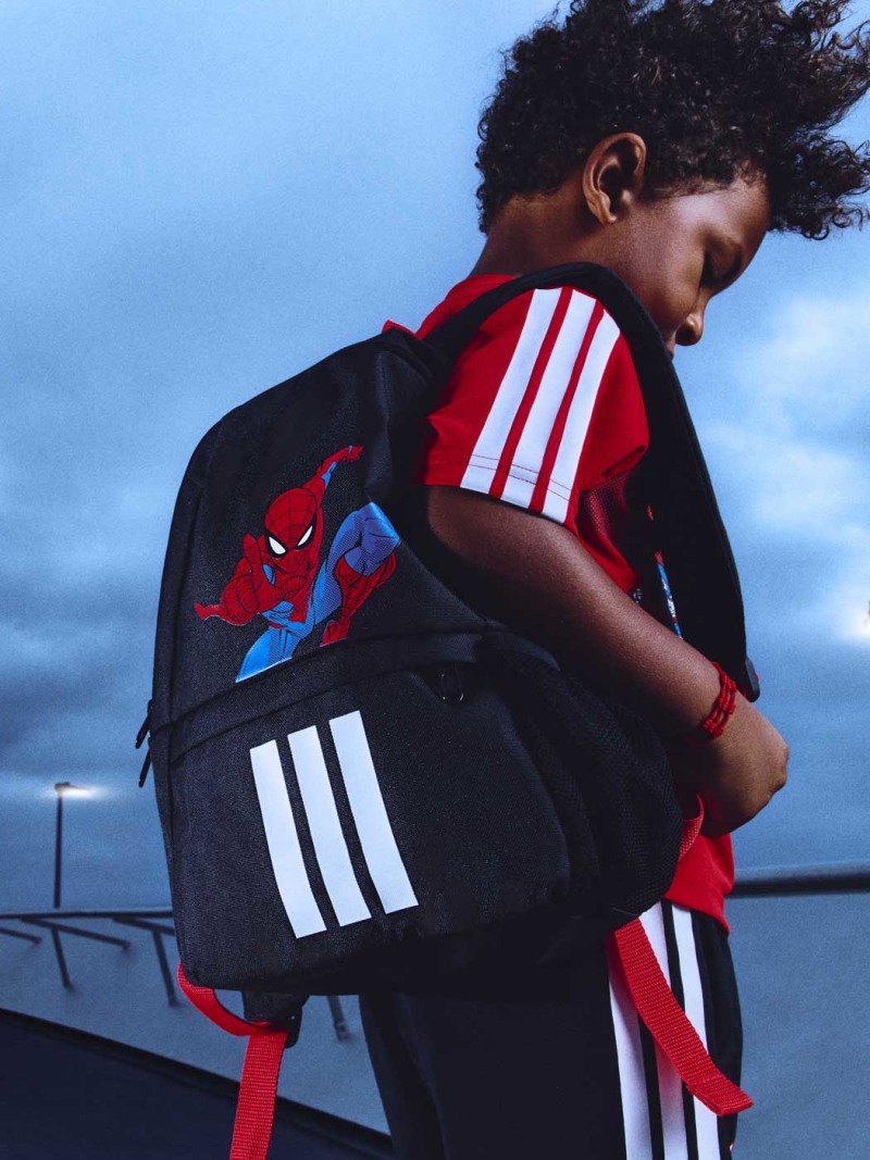 A young person wearing a backpack with a Spider-Man design, standing in front of a body of water and a cloudy sky.