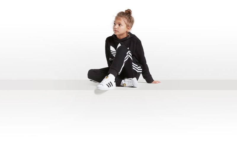 A young girl wearing a black and white athletic outfit sits on a plain white background, her hair styled in a bun on top of her head.