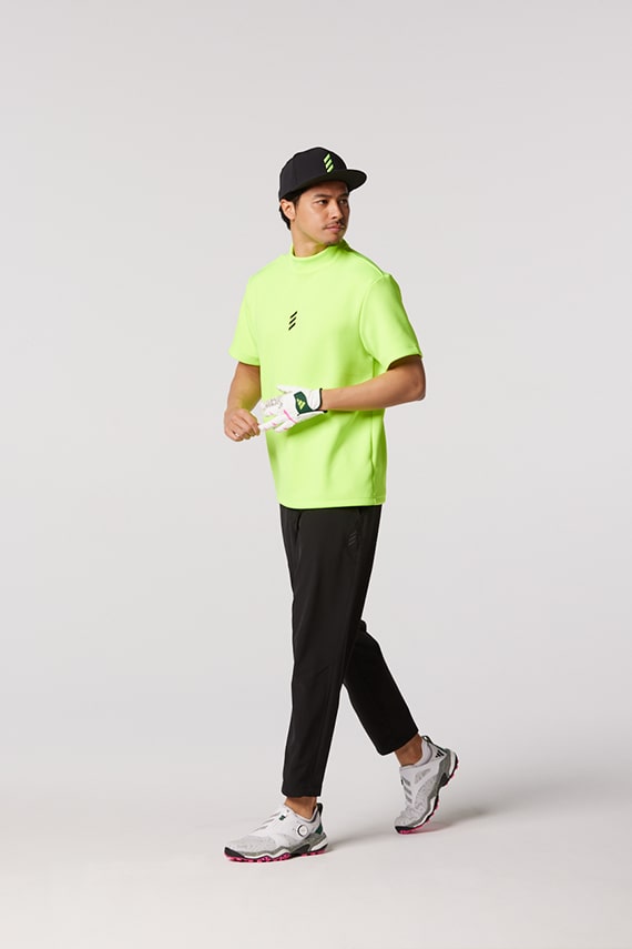 A person wearing a neon green t-shirt, black cap, and sneakers is standing against a plain white background.