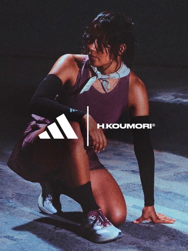 A person wearing athletic clothing and gear, including an Adidas H.Koumori logo, is crouched on a dark stage or floor.
