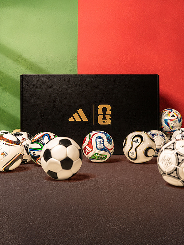 An assortment of soccer balls and an Adidas box on a dark surface, set against a vibrant green and red background.