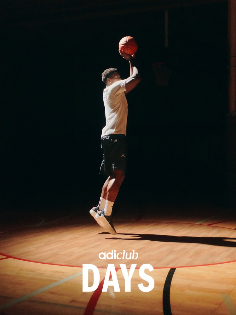 A person in athletic clothing is jumping and holding a basketball on a basketball court with the "adiclub DAYS" logo visible in the background.