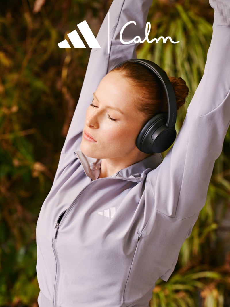 A person wearing a gray hoodie and headphones appears to be relaxing in a natural outdoor setting with lush greenery in the background.