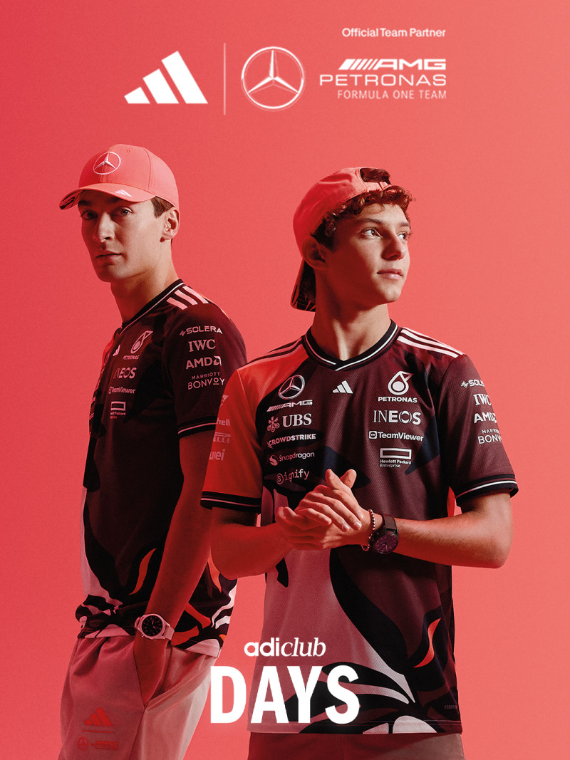 Two individuals wearing red and black uniforms with the Mercedes-AMG Petronas Formula One Team logo, standing in front of a red background.