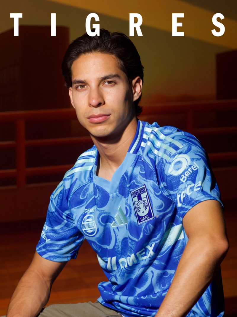 The image shows a young man wearing a blue and white patterned jersey, standing in front of a wall with the word "TIGRES" displayed prominently.