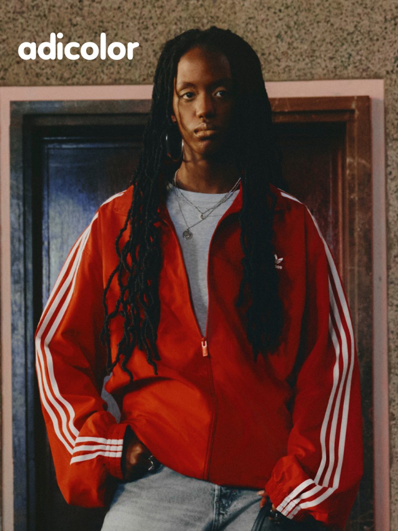 The image shows a person wearing a red jacket with white stripes, standing in front of a wooden door.