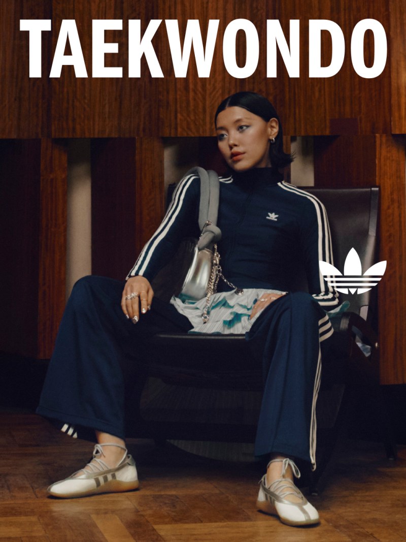 A person wearing a black Taekwondo uniform and Adidas sneakers is sitting on a wooden bench in what appears to be a Taekwondo training facility.