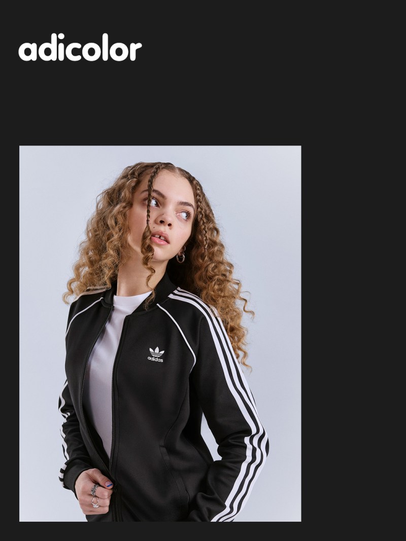 The image shows a young woman with curly hair wearing a black Adidas jacket against a plain black background.