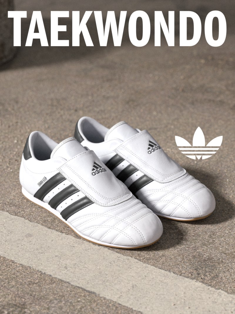 The image shows a pair of white Adidas sneakers with black stripes, placed on a concrete surface against a plain background with the word "TAEKWONDO" prominently displayed.