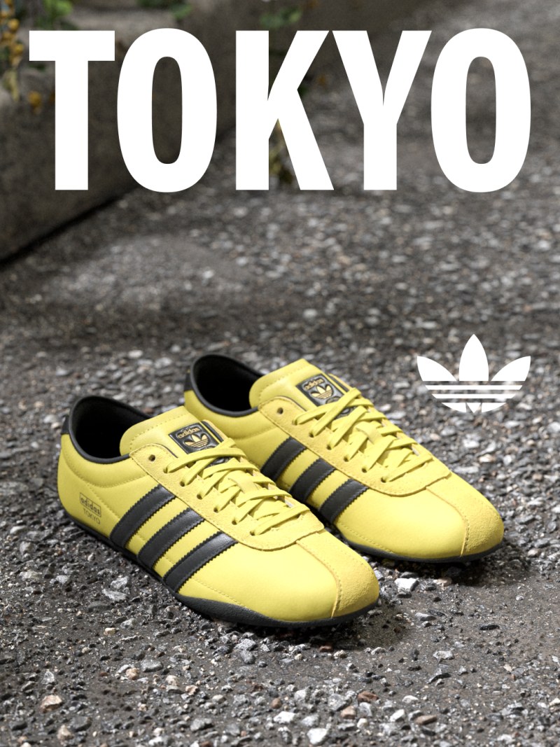 A pair of yellow Adidas sneakers sits on a wet, paved surface against a blurred background featuring the word "TOKYO" in large white letters.
