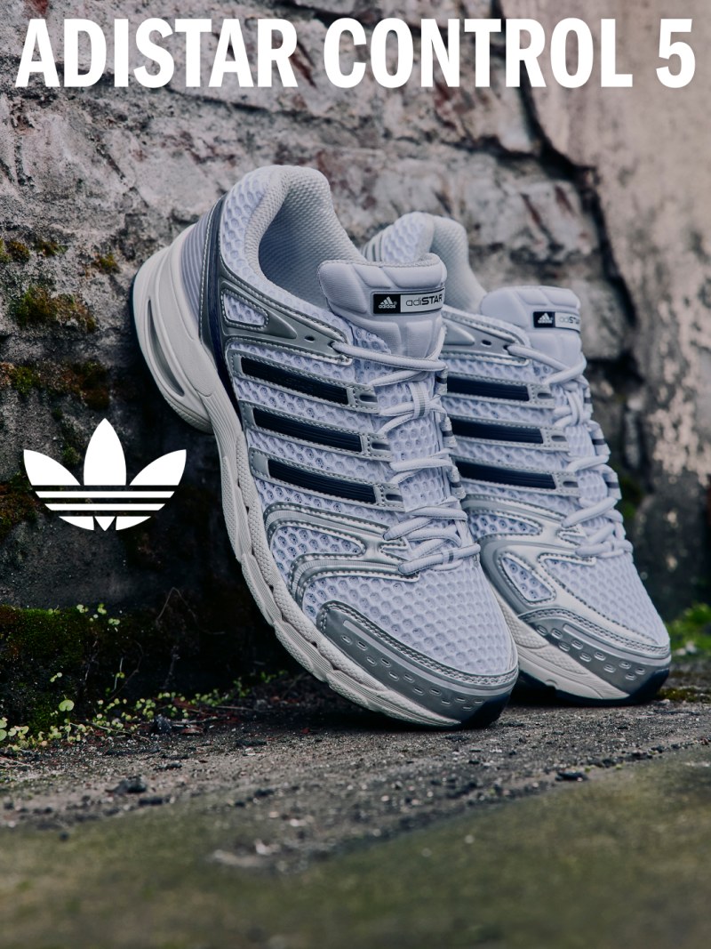 The image shows a pair of gray and white Adidas Control 5 sneakers resting on a rocky, natural surface.
