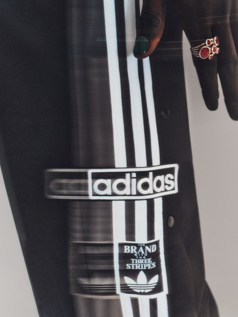 Hands with rings, part in pockets of black Adibreak track pants.