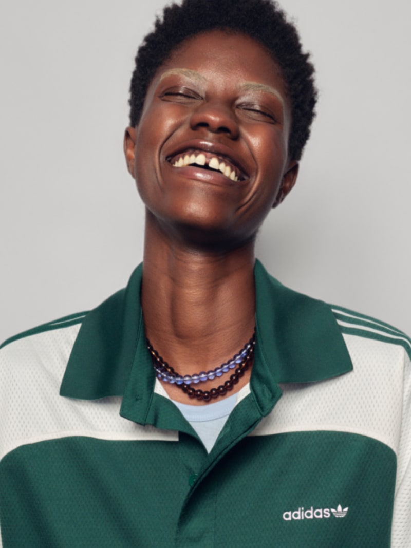 A person in profile, smiling, wears a Adidas polo  