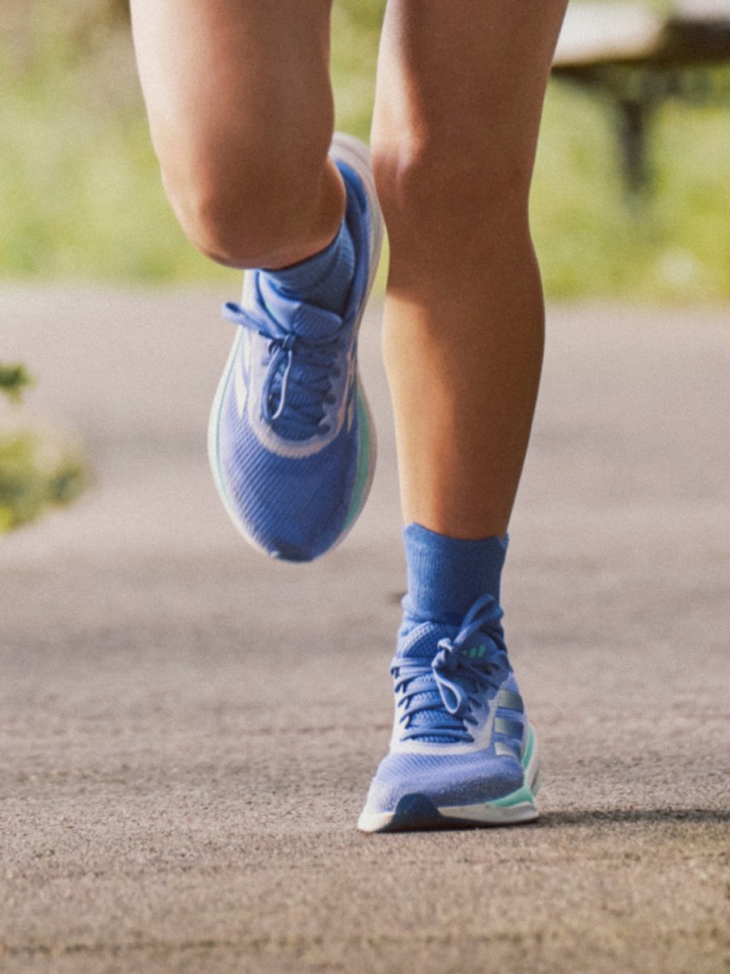 The blue and turquoise adidas Supernova Stride running shoes pictured on-foot on an asphalt street.