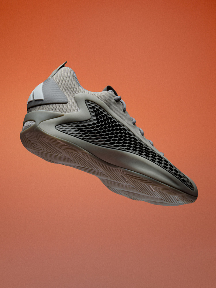 A gray and black athletic shoe with a textured sole is displayed against a vibrant orange background.