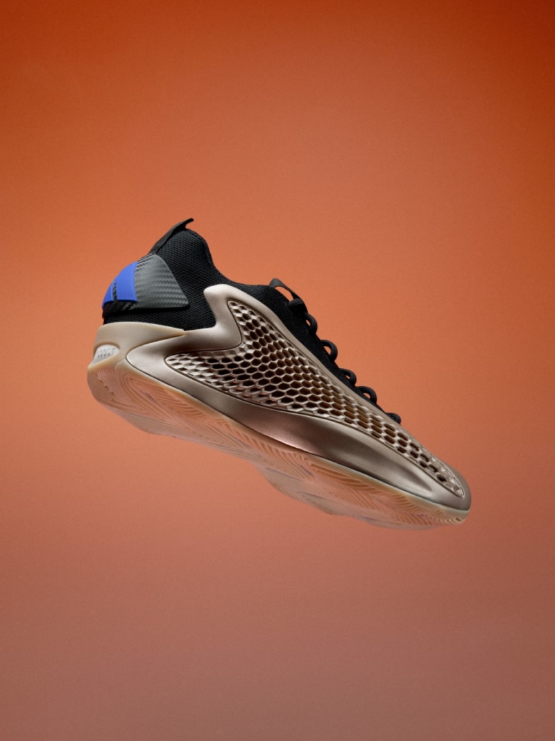 A sleek, futuristic-looking sneaker with a textured, perforated upper and a distinctive sole design against a vibrant orange background.