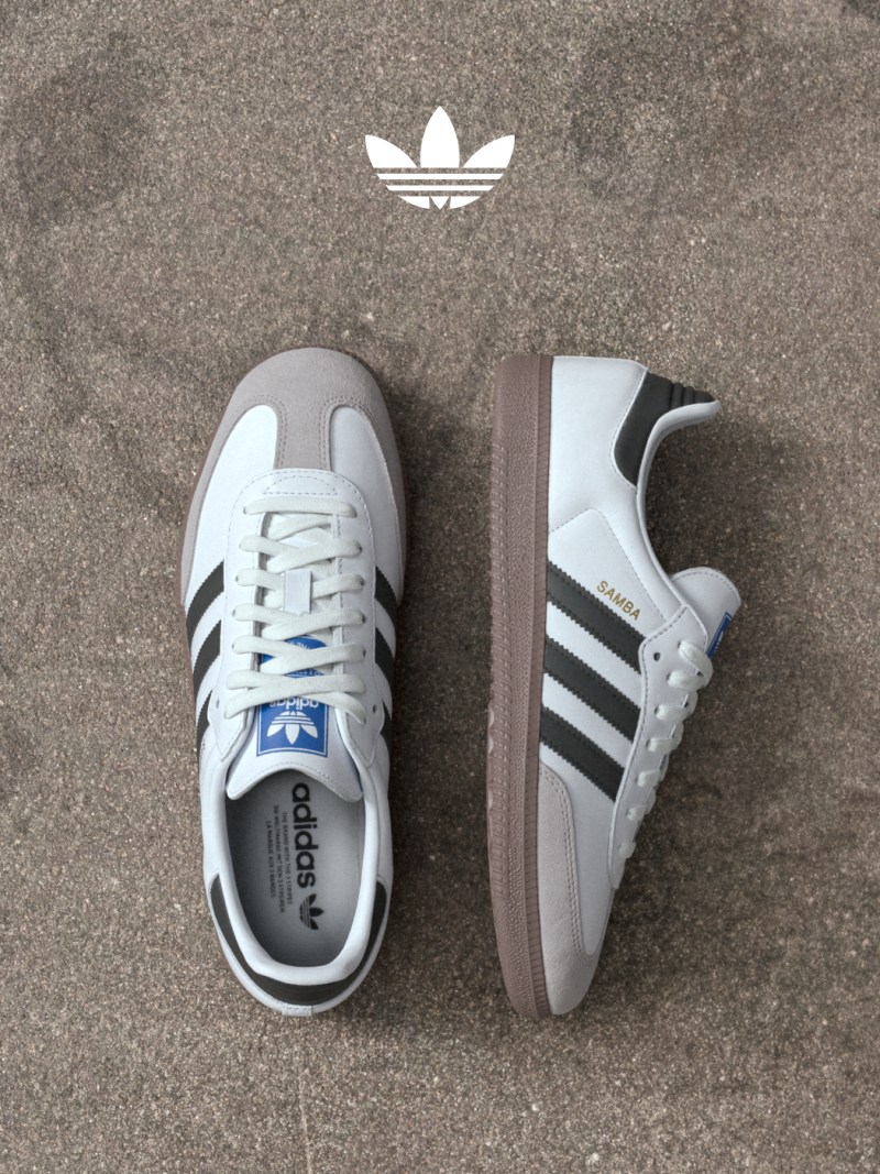 A pair of white and gray Adidas sneakers with the iconic Adidas logo visible, resting on a gray concrete surface.