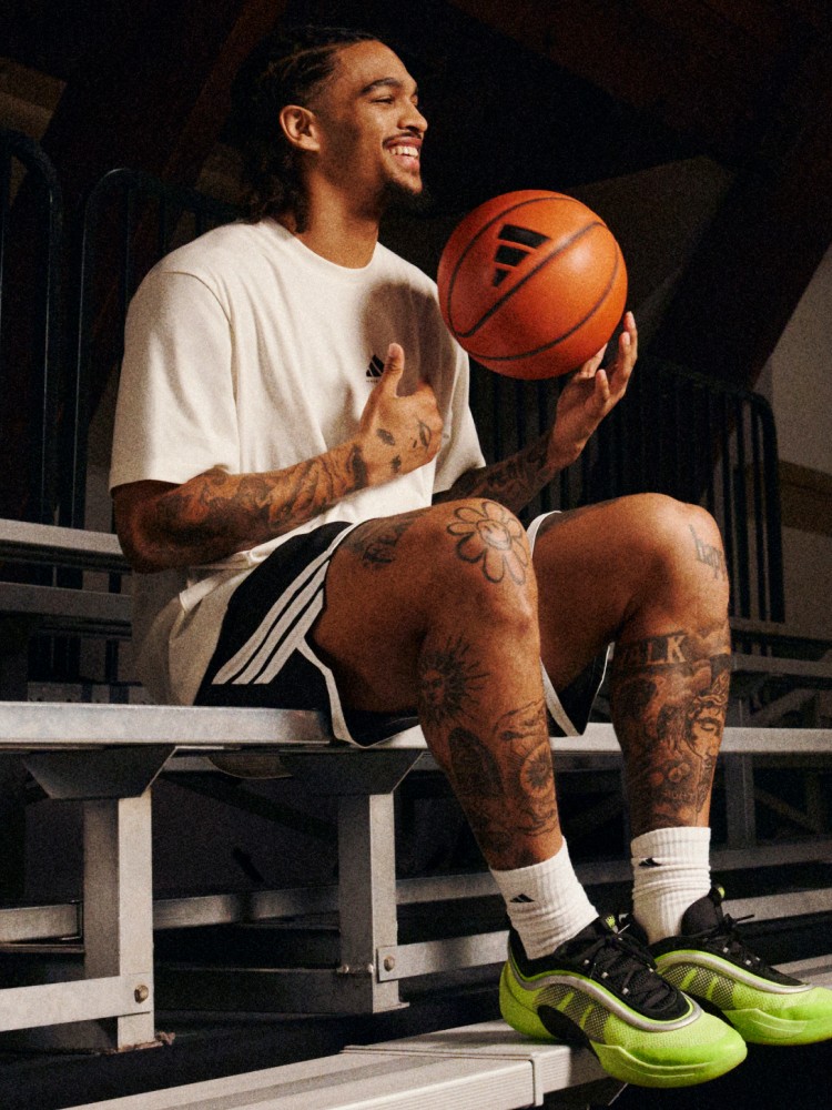 A young man with tattoos sits on a bench, holding a basketball and smiling at the camera.