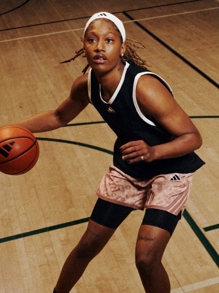 A young woman in athletic clothing is dribbling a basketball on a wooden basketball court.
