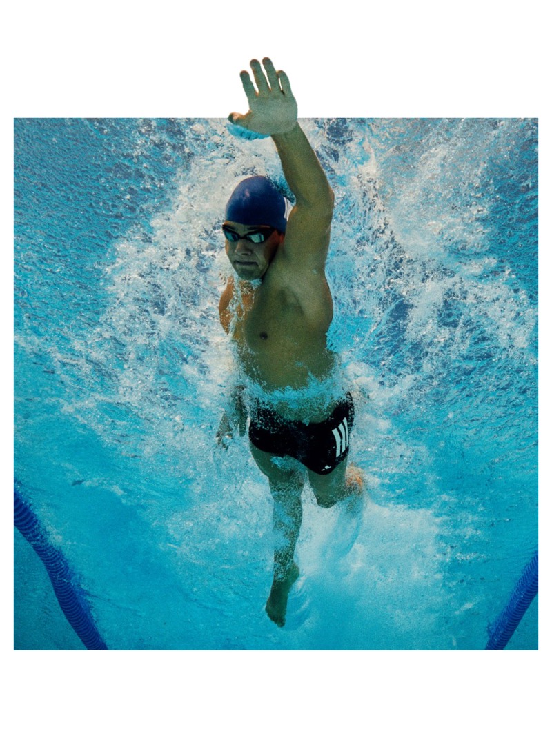 A person wearing a swim cap and goggles is swimming underwater in a pool, with water splashing around them.