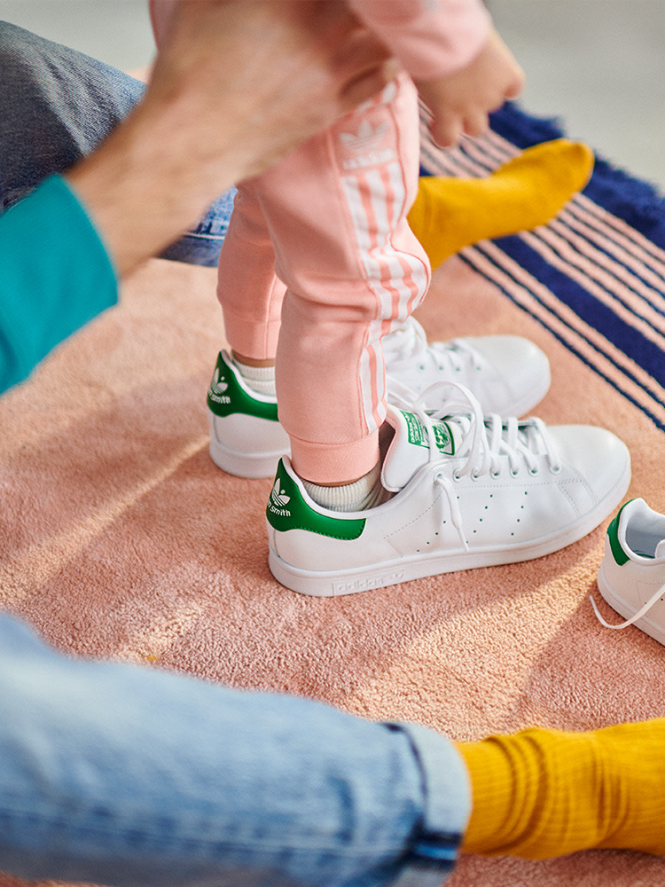 The image shows a person's feet wearing white sneakers with green accents, sitting on a pink and blue striped blanket or rug.