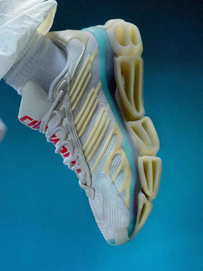 The image shows a close-up view of a white and yellow athletic shoe with a distinctive sole design against a vibrant blue background.