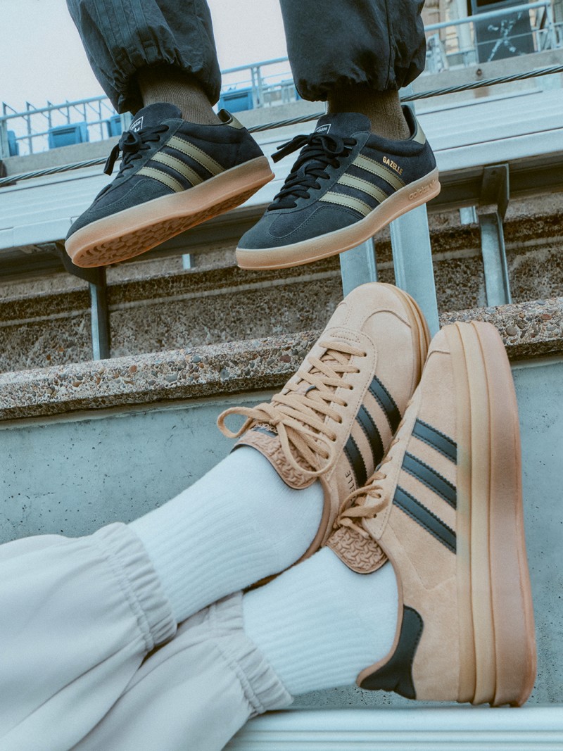 The image shows a pair of sneakers, one black and one beige, on a person's feet. The background appears to be a concrete surface, possibly a sidewalk or a platform.