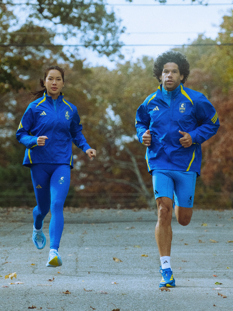Two people, a man and a woman, are jogging together on a path surrounded by trees and foliage in an outdoor setting.